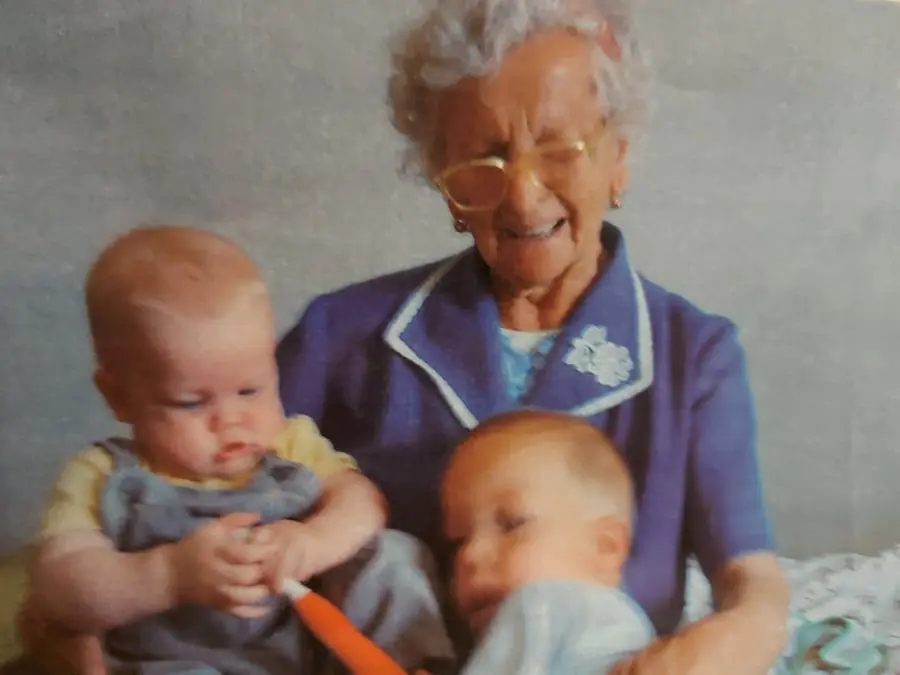 Grandma in glasses laughing, holding two baby boys on her lap