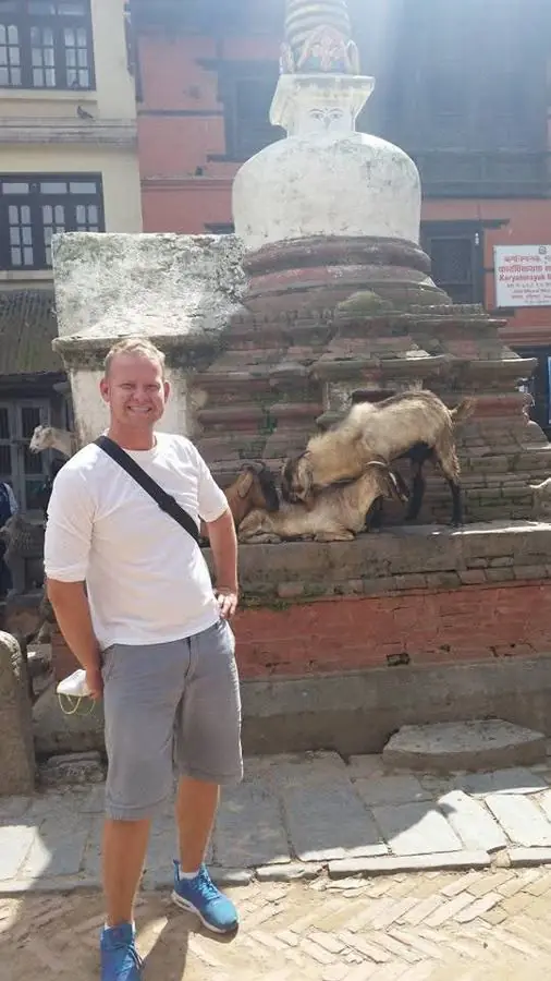 Me standing in front of a white stupa with goats resting on its brick base