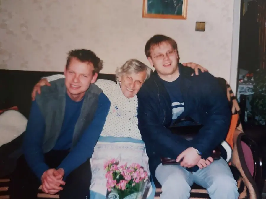 Grandma smiling between two of us, with a bouquet of pink flowers on the table