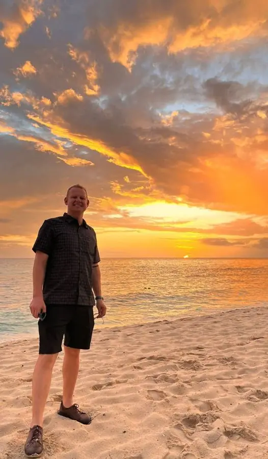 Me on a beach at sunset, with an orange sky over the sea